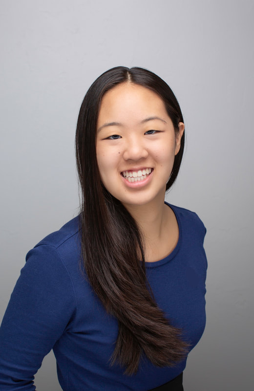 A picture of Jane Huang. She is facing the camera and smiling. Her background is gray and she is wearing a navy blue shirt. Her long, dark brown hair is down, with part of her hair swept back and the rest hanging down past her left shoulder.
